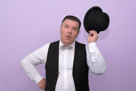 Portrait of surprised man in a retro suit. Bowler hat, white shirt and black vest. Light purple backgroundの写真素材