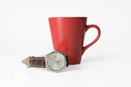 Time for coffee. Red mug and wrist watch on a strap on a white background. mockup, closeup. selected focus on the watchの写真素材