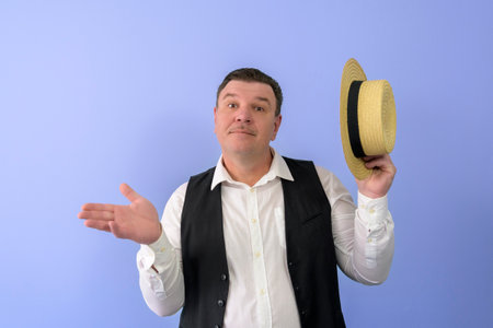 What did a man look like in the 1920s? Portrait of a man in a white shirt, black vest and with a straw hat in his hands. Lilac backgroundの写真素材