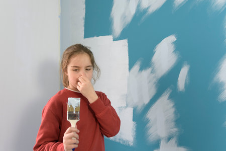 The girl covers her nose and winces at the smell of the stench of harmful paint while painting the wall.の写真素材