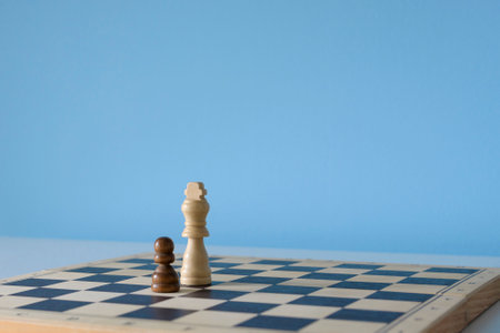 White chess king and black pawn on a chessboard on a light blue backgroundの写真素材