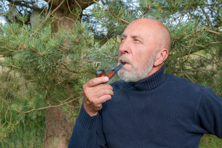 An elderly retired man enjoys nature in the forest. Senier smoking a pipe in natureの写真素材