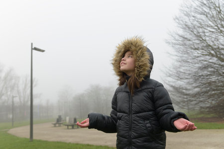 Waiting for snow. Portrait of a girl in cold weather in a warm jacket with a fur hood. Place for textの写真素材