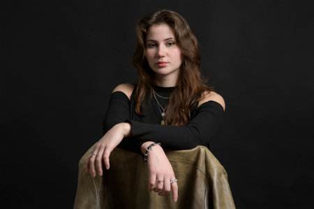 Studio portrait of a young lady on a black background sits on a chair with a leather jacket. Caucasian. Brunette. piercingの写真素材