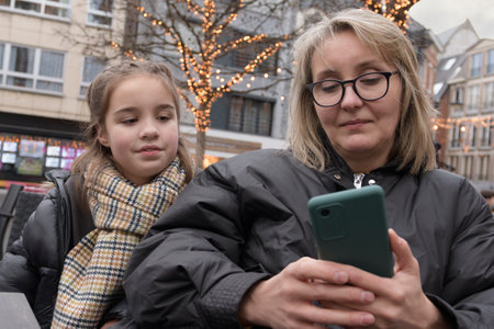 Mom and daughter on a walk in the festive Christmas city, looking through new selfies on a...
