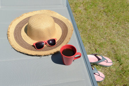Red sunglasses, straw hat, coffee mug close-up on sun loungerの写真素材