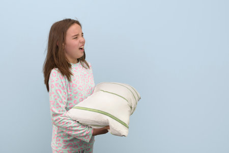 Girl yawns, with a pillow in her hands, in pajamas and disheveled hair. Light green backgroundの写真素材
