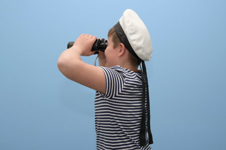 Sailor boy on a light blue background. A teenage boy in a sailor suit with a binocular looking to the leftの写真素材