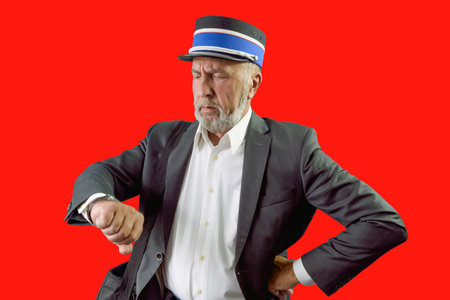 The postman looks at his watch. Red background. Isolated. Portrait of an elderly postmanの写真素材