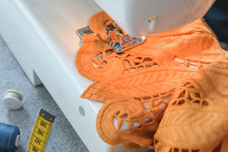 Orange lace fabric being processed on a sewing machine in the process. Close-up