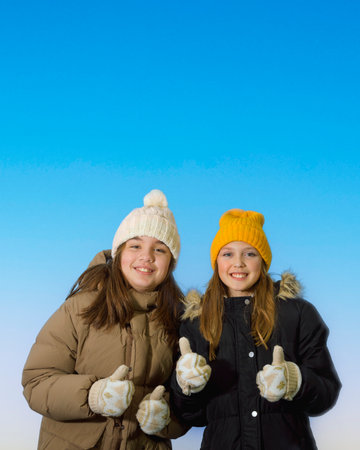 Two girlfriends portrait in winter clothes. Winter motif and clothes. studio photo. Sweaters, scarves, gloves. Joy on the faces. On blue backgroundの写真素材