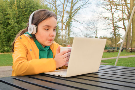 With a laptop and a cup of coffee, a teenage girl sits at a table