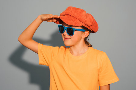 A young girl wearing a yellow shirt and blue sunglasses is looking up at the sky. She is wearing a red hat and has a smile on her face. Concept of fun and playfulnessの写真素材