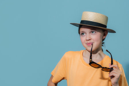 A young girl wearing a straw hat and holding a pair of sunglasses. She is smiling and looking at the cameraの写真素材
