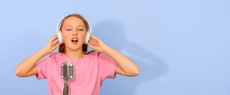 A teenage girl sings a song in the studio with a microphone and headphones. Mockup, copy space. Banner. blue backgroundの写真素材