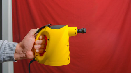 A vacuum cleaner. A person is holding a yellow steam cleaner. Red background. The person is holding the device with one handの写真素材