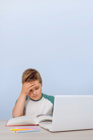 Portrait of a 10-12 year old boy at a desk with a book and a computer. Boy reading a book