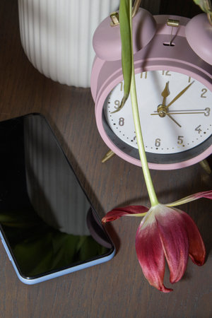 Silent smartphone on the table with a pink alarm clock and withered tulip close-up