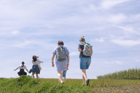 A group of people are walking on a grassy hill, with one woman wearing a backpack. Scene is peaceful and relaxed, as the group of people are enjoying a leisurely walk togetherの写真素材
