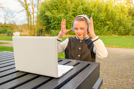 Teenage girl surprised at table with laptop and white headphones in park at table