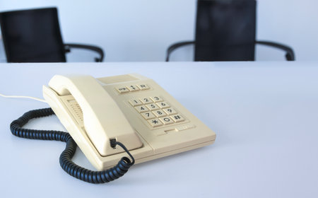 A white phone 80s - 90s with a cord hanging off it sits on a table in officeの写真素材