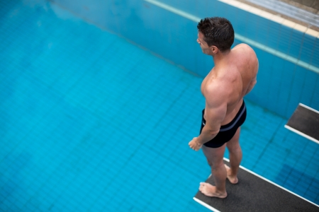 Man standing on diving board at public swimming pool above the waterの写真素材