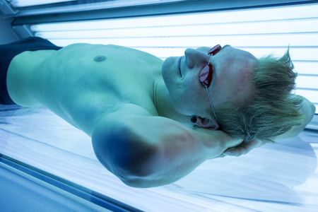 Attractive man in solarium enjoying sunbathing on tanning bedの写真素材