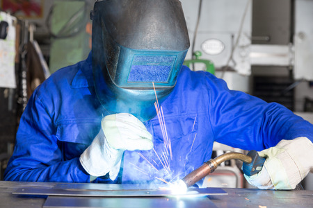 professional welder welding metal pieces with light arc and sparks