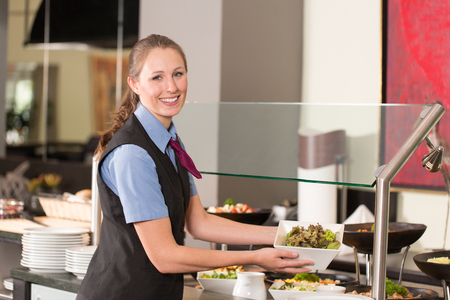 Waitress or catering professional putting food into a buffetの写真素材
