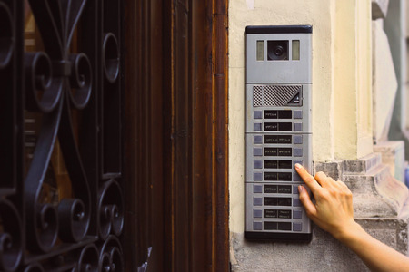 The girl is pressing by finger on the intercom's button with a camera near a beautiful old wooden doorの写真素材