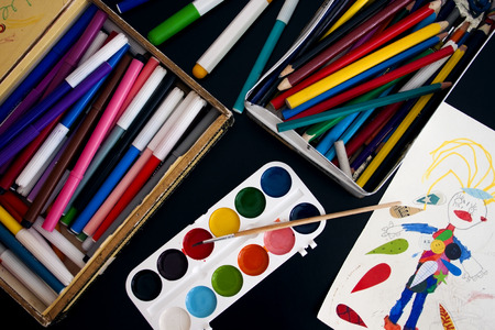 Children's paints, pencils, markers and drawing on the black tableの写真素材