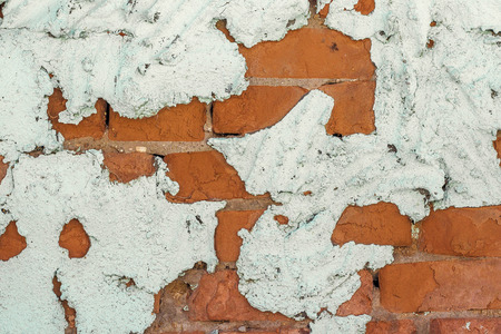 old brick wall behind a layer of crumbling painted plaster, background or textureの写真素材