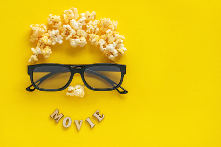 Abstract image of viewer, 3D glasses and popcorn,  text  "movie" on yellow background. Still life, top view, flat lay. Concept cinema and entertainmentの写真素材