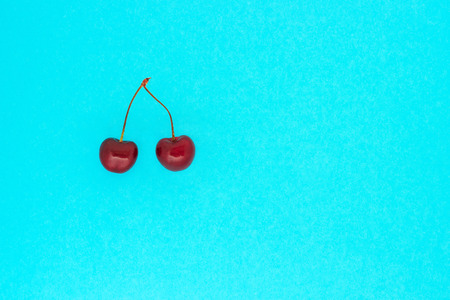 two ripe red cherries on blue background, top view, minimalism, copy space の写真素材
