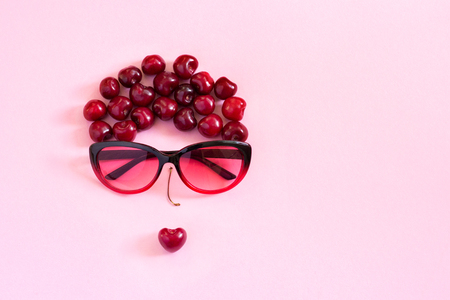 abstract image young woman from sweet cherry and glasses on pink background.  Concept - youth, beauty, summer Still life Top view Flat lay Copy spaceの写真素材