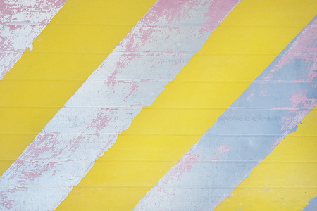 old metal surface with peeling pink paint and yellow diagonal stripes, texture, backgroundの写真素材