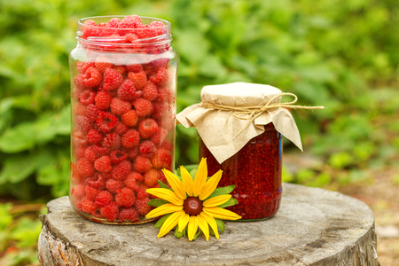 Harvest Raspberry berries in the glass jar, Jam and flower on old stump, sunny summer day vegetable...