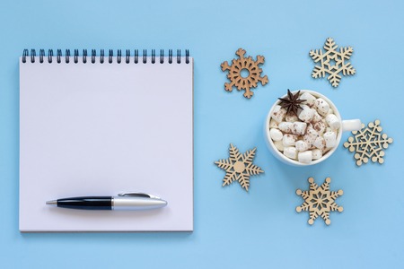 Winter composition. Cup of cocoa with marshmallow and star anise, empty open notepad with pen and snowflake on blue background. Top view Flat lay Mockup Conceptの写真素材
