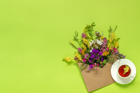 Field colorful rustic vintage flowers in craft envelope and cup of herbs tea on green background Greeting card Flat Lay Copy space Concept Hello Spring or Summer.の写真素材