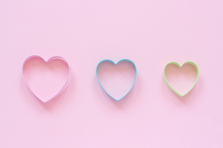 3 colorful cutters cookies in heart shape on pastel pink background. Concept Valentine's card. Top view Copy space for text.の写真素材