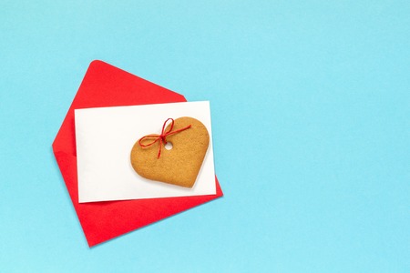Red envelope with blank white card for text and heart shaped ginger cookies on blue background. Top view Copy space Mock up Concept letter greetings with loveの写真素材