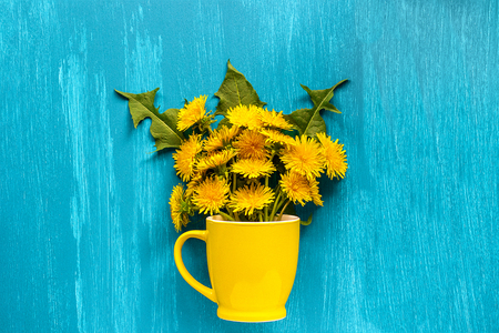 Bouquet dandelions taraxacum flowers in yellow mug on wood blue background Template for postcard, lettering, text or your design Flat lay Top view Concept Hello summer Creative top-down composition.の写真素材