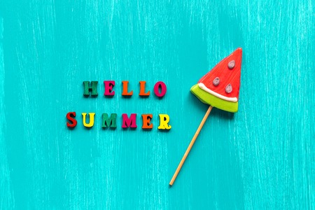 Hello summer text from colorful letters and watermelon lollipop on stick on wooden blue background. Concept Creative Top view Template Greeting card.の写真素材