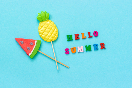 Hello summer colorful text, pineapple and watermelon lollipops on stick on blue paper background. Concept vacation or holidays Creative Top view Template Greeting card, postcard.の写真素材