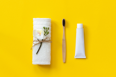 Natural eco-friendly bamboo brush, white towel and tube of toothpaste. Set for washing on paper yellow background. Copy space for text or your design Top view Flat lay.の写真素材