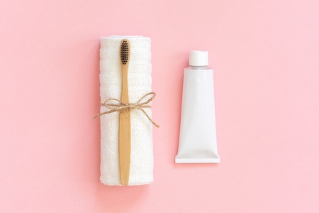 Natural eco-friendly bamboo brush on white towel and toothpaste tube. Set for washing on paper pink...