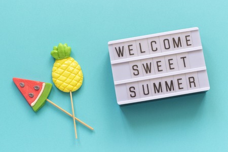 Welcome sweet summer text on light box, pineapple and watermelon lollipops on stick on blue background. Concept Hello summer Creative Top view Template Greeting card, postcard.の写真素材