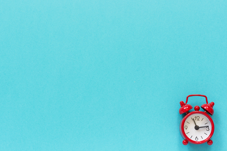 Red alarm clock in lower right corner on blue paper background. Minimal style Copy space Top view...