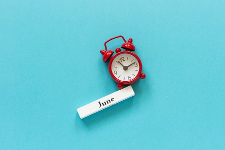 Wooden calendar summer month June and red alarm clock on blue paper background. Concept Hello June or Good bye June Creative Top view Flat Lay Minimal style.の写真素材