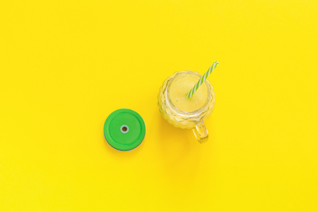 glass jar with natural yellow fruit juice, smoothie or fresh with green lid and cocktail straw on yellow background. Top view Copy space Template.の写真素材